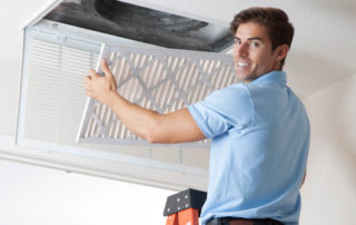 Professional air duct cleaner in a blue shirt cleans an air duct.