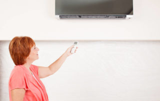 Woman holding a remote control air conditioner at home.