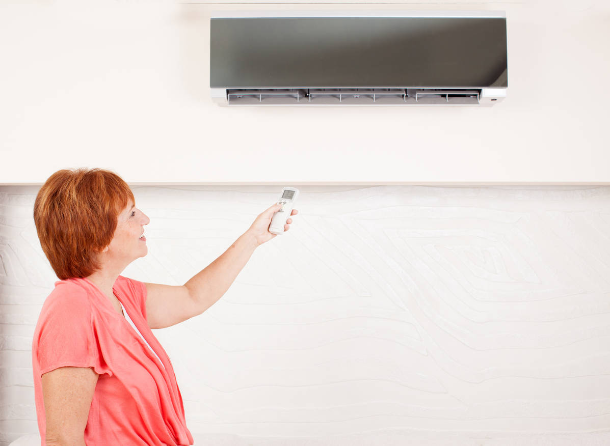 Woman holding a remote control air conditioner at home. Happy mature woman on sofa