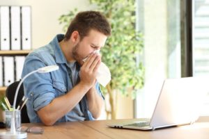 A man sneezing in front of a laptop