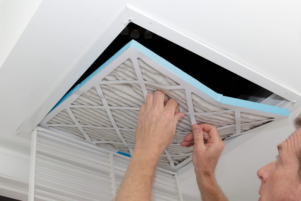 Person Removing an Old Dirty Air Filter From a Ceiling Intake Vent of a Home Hvac System