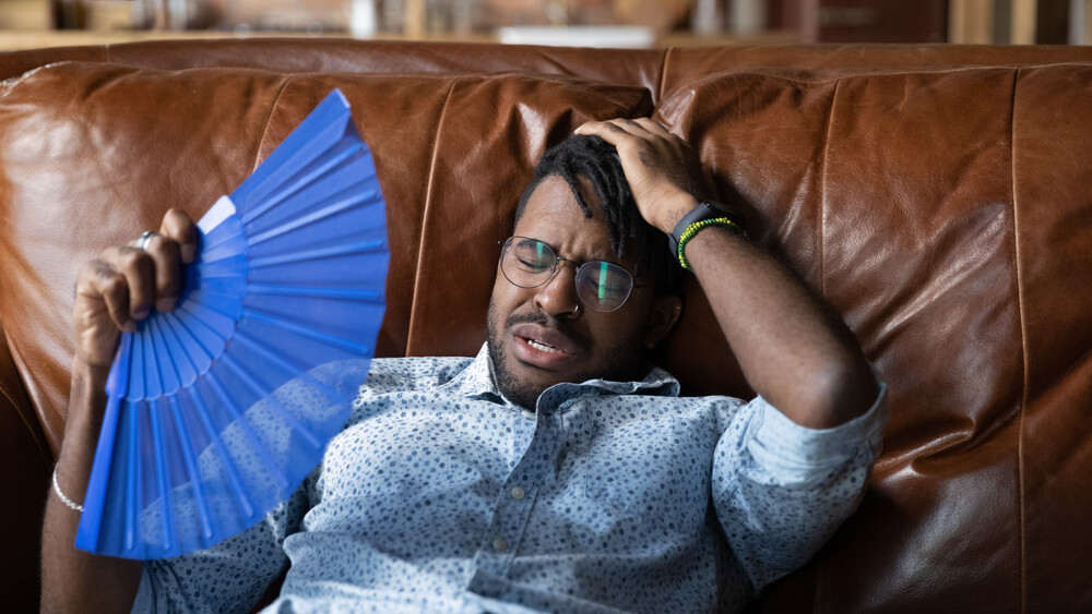 Overheated Millennial Man Recline on Couch at Home Get Heat Stroke Use Hand Fan.