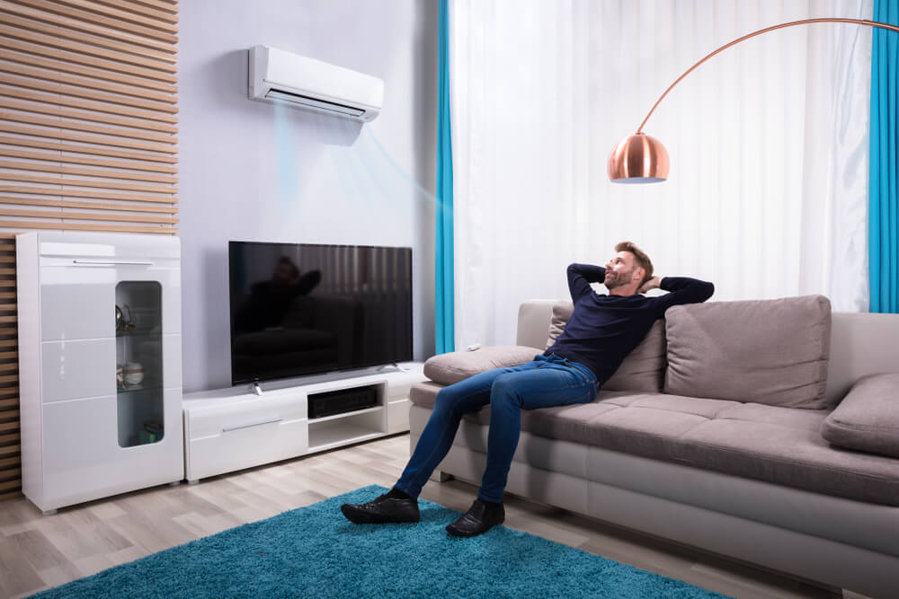 Happy Young Caucasian Woman Relax on Couch in Living Room Turn on Air Conditioner With Remote Controller