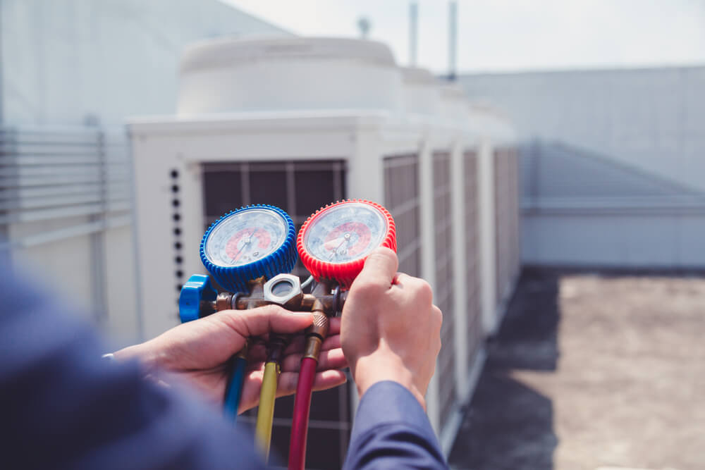 Technician using measuring manifold gauge checking refrigerant and filling industrial air conditioner.