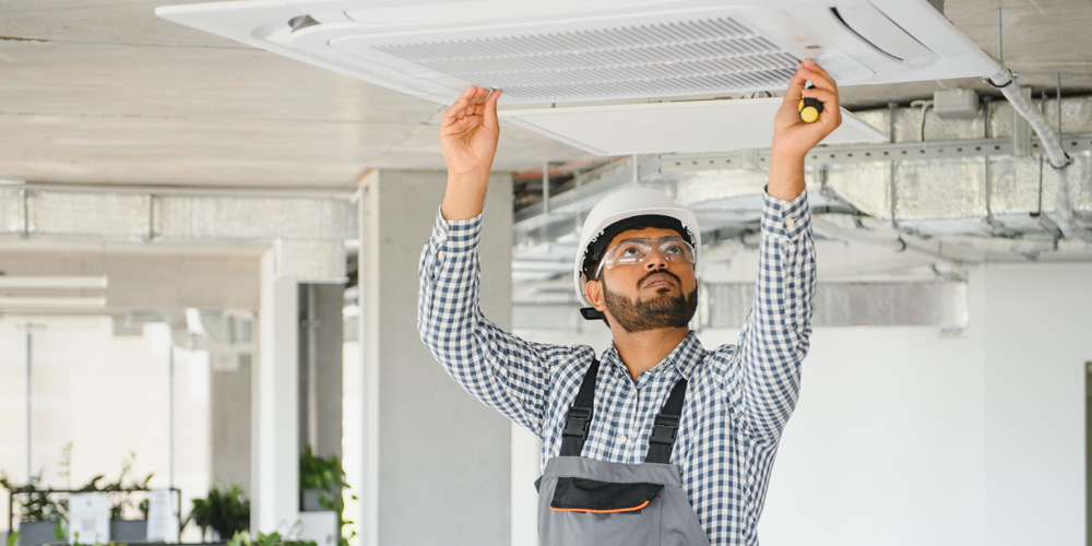 A man wearing overalls and a hard hat is working on fixing an air conditioner demonstrating skilled maintenance | Chills AC