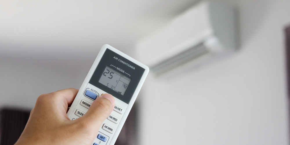 Individual using a remote control to adjust settings on a wall air conditioning unit | Chills AC