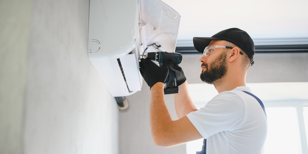 A man wearing a hat and gloves repairs a wall-mounted air conditioner | Chills AC