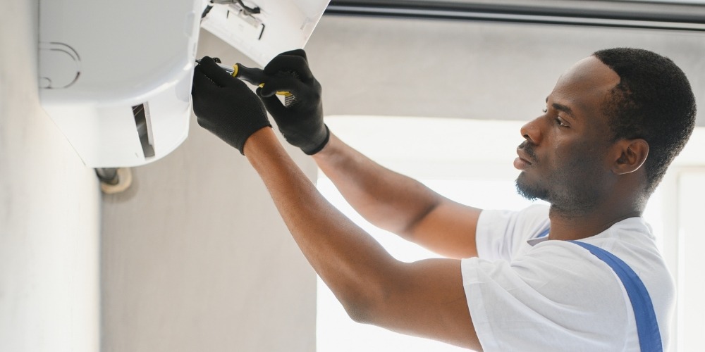 A man in a white shirt and gloves repairs an air conditioner focused on the units internal components | Chills AC