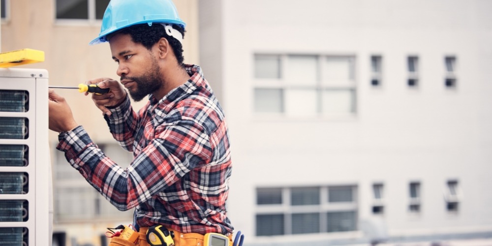A man wearing a hard hat and safety vest repairs an air conditioner on a rooftop | Chills AC