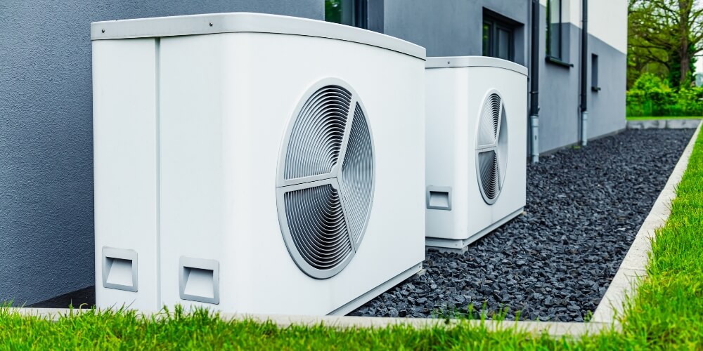 Two air conditioning units installed outside a residential house | Chills AC Outdoor air conditioning condenser units mounted against a modern building on a gravel strip with a green lawn nearby.