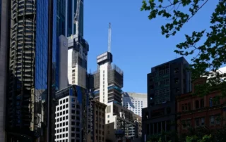 Downtown street lined with tall glass office buildings under construction against a blue sky with a crane visible above.